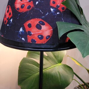 May include: A black table lamp with a black and red ladybug print lampshade. The lamp base is black and features a ladybug figurine.