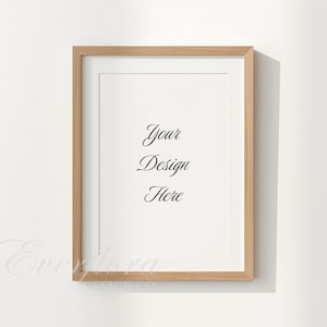 May include: A vertical rectangular picture frame with a light brown wood grain finish and a white mat board. The center of the frame contains the black text "Your Design Here" in a cursive script font. The frame is displayed against a plain white wall.