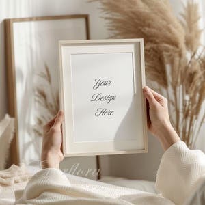 May include: A light beige rectangular picture frame with a white mat board. The center of the frame contains the black printed text Your Design Here. The frame is held upright, showcasing a clean, simple border and a neutral color palette.