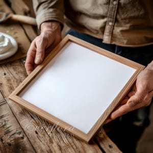 Puede incluir: Un marco de fotos rectangular de madera con acabado marrón claro y un inserto central blanco liso. El marco presenta un diseño de borde liso y limpio. El texto Everflora Design Co es visible en letra cursiva en la esquina inferior izquierda.