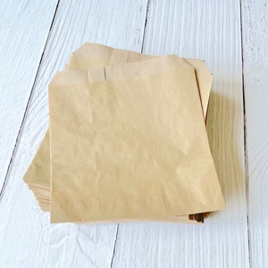 May include: A stack of brown paper bags on a white wooden surface.
