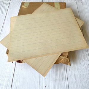 May include: Two sheets of lined paper, both are beige with blue lines, stacked on top of each other. The paper is folded in half and the top sheet is slightly lifted.