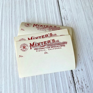 Könnte beinhalten: Drei vintage Rezeptblöcke von Mixter's Pharmacy in Visalia, Kalifornien. Die Blöcke sind cremefarben mit roter Tinte und tragen das Logo der Apotheke, das die Worte "Mixter's Pharmacy" und "Prescription Specialists" enthält.