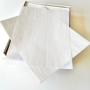 Może przedstawiać: Stos białych arkuszy papieru jedwabnego w kartonowym pudełku. Papier jedwabny jest złożony i ułożony w kształcie tr&oacute;jkąta.