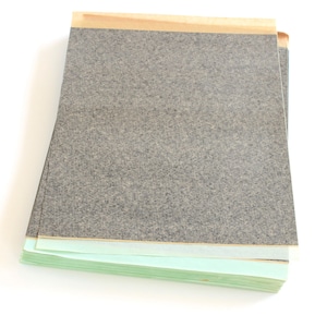 May include: A stack of black carbon paper with a brown paper backing and green paper backing.