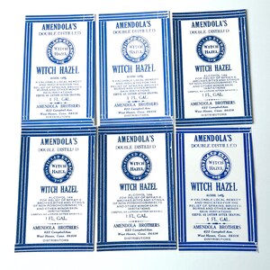 Op de afbeelding: Zes vintage-etiketten voor Amendola's Double Distilled Witch Hazel. Elk etiket heeft een blauw en wit ontwerp met een cirkelvormig logo van een toverhazelaarplant en de tekst "Witch Hazel" in een witte banner. De etiketten bevatten ook de tekst "Amendola's Double Distilled" en "Alcohol 14%".