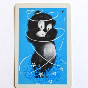 K&ouml;nnte beinhalten: Ein schwarz-wei&szlig;er Comic-B&auml;r vor blauem Hintergrund. Der B&auml;r ist von wei&szlig;en Wirbeln und wei&szlig;en Blumen umgeben. Eine kleine schwarze Biene fliegt in der oberen rechten Ecke.