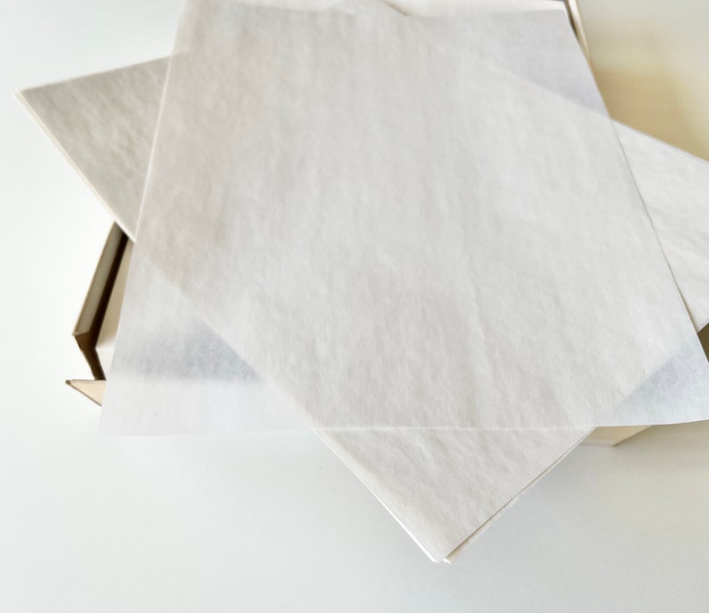 Może przedstawiać: Biały papier jedwabny złożony w kształt kwadratu, w pudełku kartonowym.