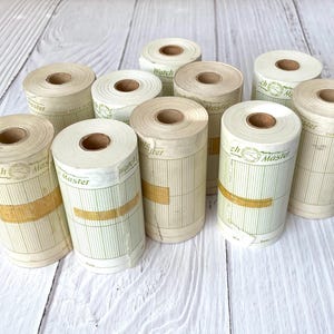 May include: A collection of vintage chart paper rolls, labelled "Watch Master Chart Paper". The rolls are cream-coloured with vertical lines and a gold band. The paper is rolled around a brown cardboard core.