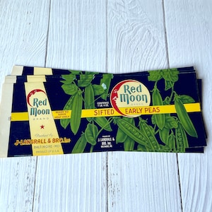 May include: Vintage Red Moon brand early peas label with a red moon and a star. The label is blue with yellow text and features a picture of green peas in pods. The text reads "Red Moon Brand SIFTED EARLY PEAS".
