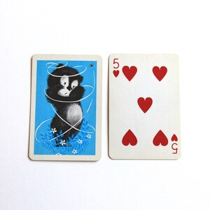 K&ouml;nnte beinhalten: Eine Spielkarte mit einer Schwarzwei&szlig;illustration einer Katze, die sich in einer Schnur verheddert hat, auf blauem Hintergrund. Die Karte ist eine F&uuml;nf Herz.