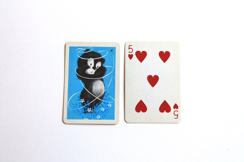 K&ouml;nnte beinhalten: Eine Spielkarte mit einer Schwarzwei&szlig;illustration einer Katze, die sich in einer Schnur verheddert hat, auf blauem Hintergrund. Die Karte ist eine F&uuml;nf Herz.