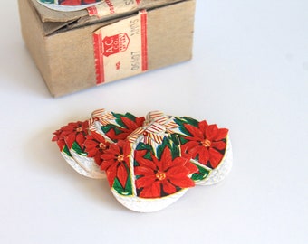 Könnte beinhalten: Ein Set aus fünf Vintage-Weihnachtsornamenten mit roten Weihnachtssternen, grünen Blättern und weißen Akzenten. Die Ornamente sind aus Papier und haben einen weißen Hintergrund.