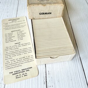 May include: A white box with a stack of flashcards inside. The box has the word "GERMAN" printed on the front. The flashcards are labeled with an explanation of the card types and abbreviations. The box is labeled "The Visual Education Association Inc. 230 W. 5th St. Dayton 2, Ohio."