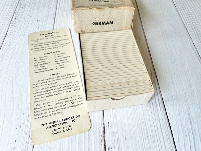 May include: A white box with a stack of flashcards inside. The box has the word "GERMAN" printed on the front. The flashcards are labeled with an explanation of the card types and abbreviations. The box is labeled "The Visual Education Association Inc. 230 W. 5th St. Dayton 2, Ohio."