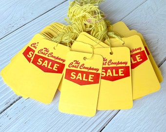 Puede incluir: Una pila de etiquetas de venta amarillas con texto rojo que dice "The Coat Company SALE".