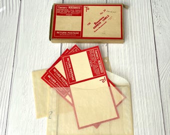 May include: A collection of vintage shipping supplies, including a box of address labels and a translucent envelope with several red and cream-colored labels. The box is labeled "Dennison Address Labels" and the labels read "Return Postage Guaranteed."