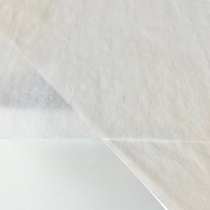 Może przedstawiać: Zbliżenie na dwa białe arkusze papieru, jeden złożony na drugim, tworząc ostry zagięcie.