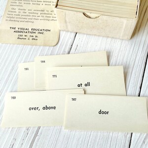 May include: A set of flashcards with numbers and words printed on them. The words include "at all", "over, above", and "door". The cards are beige and have black text. The cards are from The Visual Education Association Inc. in Dayton, Ohio.