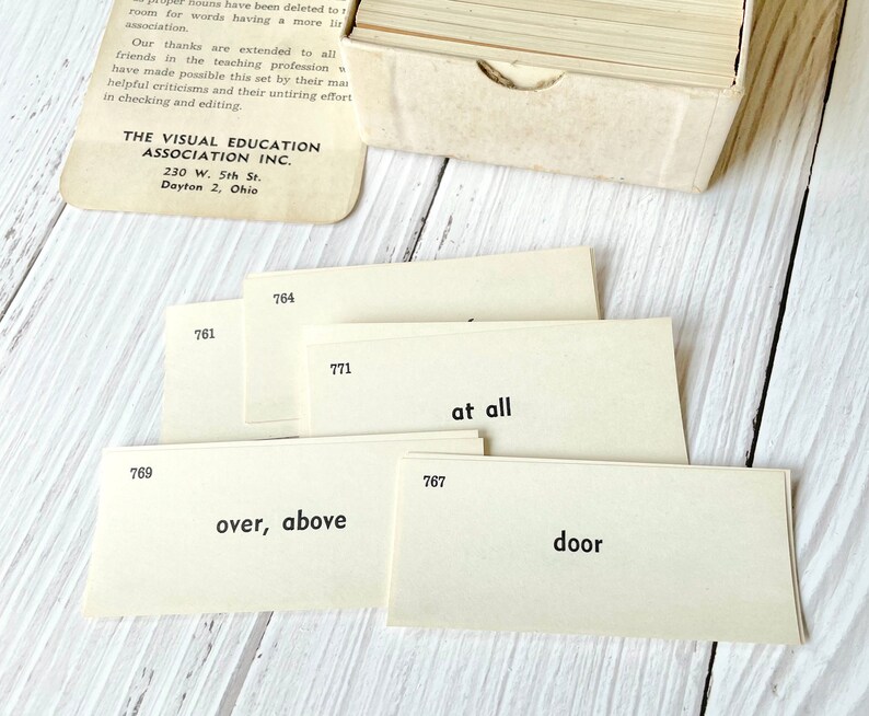 May include: A set of flashcards with numbers and words printed on them. The words include "at all", "over, above", and "door". The cards are beige and have black text. The cards are from The Visual Education Association Inc. in Dayton, Ohio.