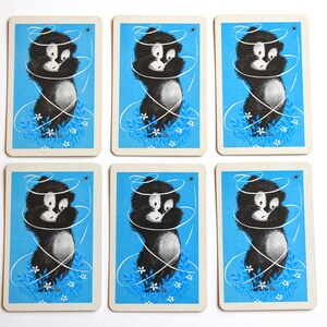 K&ouml;nnte beinhalten: Sechs Spielkarten mit blauem Hintergrund und einer Schwarzwei&szlig;illustration eines Comic-Tieres mit einem Schnurwirbel darum herum. Das Tier steht auf einem Bett aus wei&szlig;en Blumen.