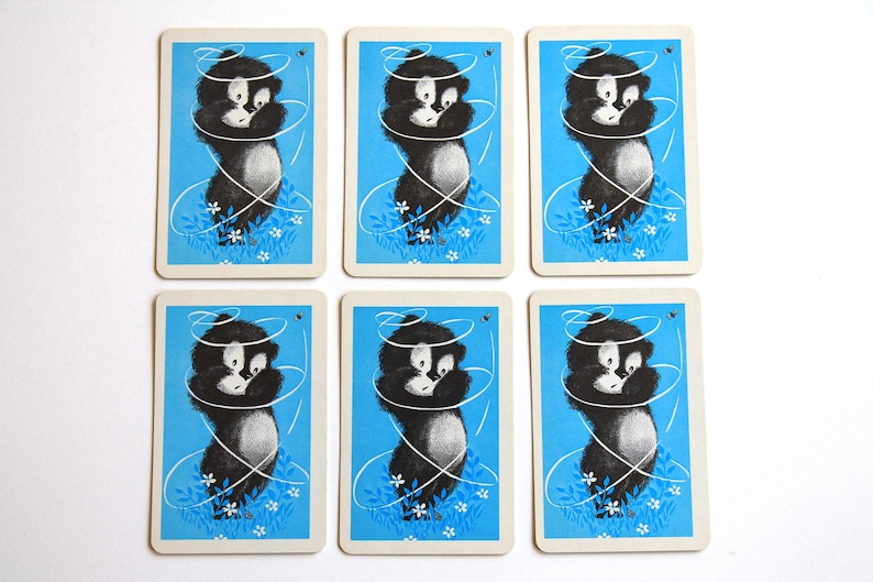 K&ouml;nnte beinhalten: Sechs Spielkarten mit blauem Hintergrund und einer Schwarzwei&szlig;illustration eines Comic-Tieres mit einem Schnurwirbel darum herum. Das Tier steht auf einem Bett aus wei&szlig;en Blumen.