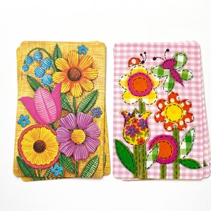 Puede incluir: Dos tarjetas con un tema floral. La primera tarjeta tiene un fondo amarillo con flores rosas, amarillas, moradas y azules. La segunda tarjeta tiene un fondo de cuadros rosa y blanco con flores amarillas, rosas, naranjas y verdes.