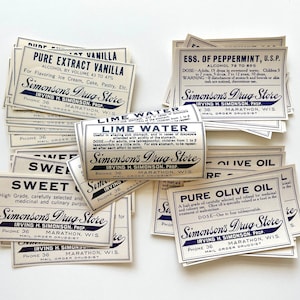 May include: A stack of vintage cream-coloured paper labels with blue text. The labels are for various products, including "Pure Extract Vanilla", "Lime Water", "Sweet Oil", "Pure Olive Oil", and "Ess. of Peppermint". All labels feature the name "Simonson's Drug Store" and the address "Marathon, Wis."