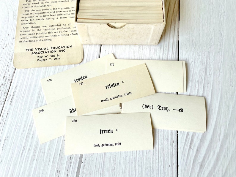 May include: Close-up of a set of flashcards with German vocabulary words. The cards are white with black text. The words on the cards include "troden", "trinken", "treten", and "(der) Tros".
