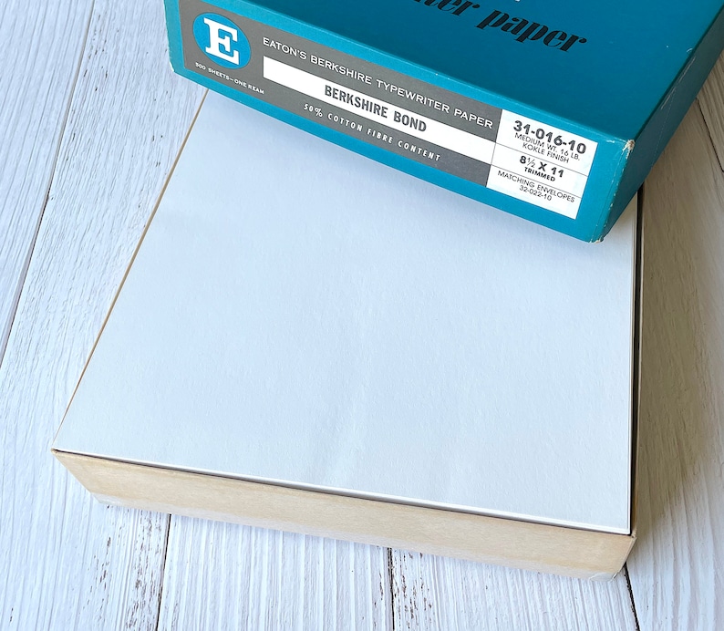以下が含まれることがあります： Eaton's Berkshire タイプライター用紙の箱。テキスト「Berkshire Bond」と「50% Cotton Fibre Content」が記載されています。箱はティール色で白い文字があり、21.6 x 27.9 cmの紙が入っています。下の箱は白で、薄茶色のトリムが付いています。