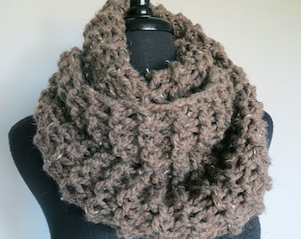 May include: A brown knitted infinity scarf made of chunky yarn. The scarf is displayed on a black mannequin.