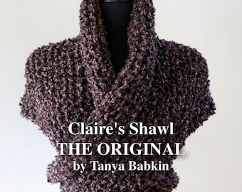 May include: A brown knitted shawl with a textured, fluffy look. The shawl is draped over a black mannequin. The text "Claire's Shawl THE ORIGINAL by Tanya Babkin" is printed on the shawl.