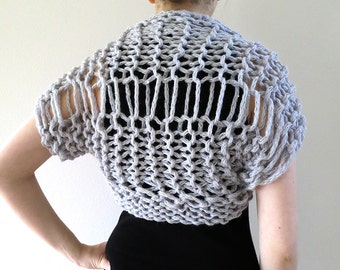 Könnte beinhalten: Eine graue Strickjacke mit kurzen Ärmeln. Die Jacke ist aus einem lockeren, offenen Maschenmuster gefertigt.