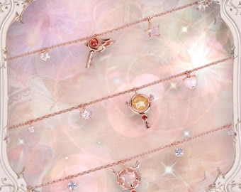 May include: Four delicate gold necklaces with charms featuring a star, a heart, and two different key designs. Each charm has a pink and white iridescent stone in the center. The necklaces are displayed against a pink and white background.