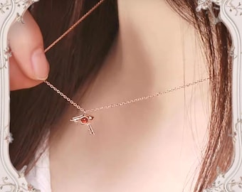 May include: A rose gold necklace with a small key pendant featuring a red gemstone eye.
