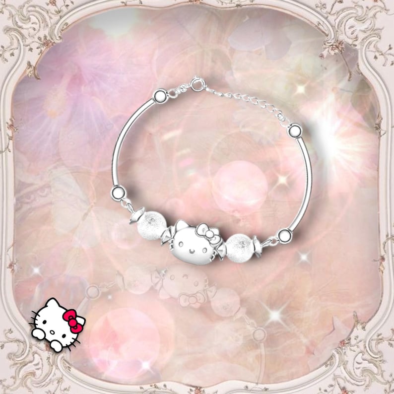 May include: A silver bracelet with a charm of Hello Kitty and white beads. The bracelet is on a pink background with a white frame.