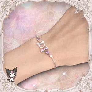 May include: A silver charm bracelet with a pink bow and a cat charm. The bracelet is on a person's wrist.
