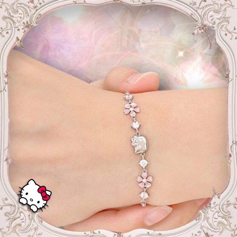May include: A silver bracelet with a pink Hello Kitty charm and pink flower accents. The bracelet is on a person's wrist.