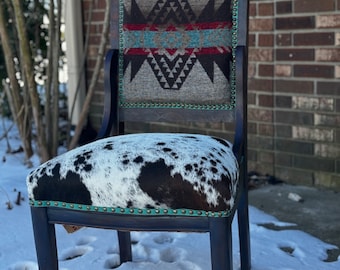 May include: A black wooden chair with a carved back and a cowhide seat. The chair is upholstered with a patterned fabric featuring geometric designs in shades of brown, gray, red, and blue.