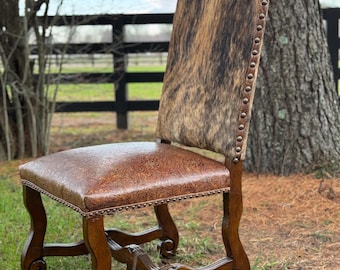 May include: A brown leather dining chair with a cowhide back and a carved wooden frame. The chair has a scrolled base and is upholstered in a brown leather with a floral pattern.