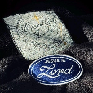 May include: Two embroidered patches on a dark gray fabric background. The top patch is white with black stitching and the text "Magical Little Butterflies". The bottom patch is blue with white stitching and the text "JESUS IS Lord".