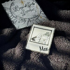 May include: Two embroidered patches. One is white with black embroidery of a photo of a person with the name Max below. The other is gray with black and gold embroidery of the text "Magical Folk & Little Eyes".