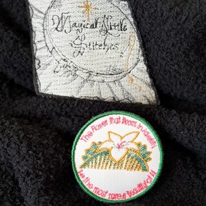 May include: A white embroidered patch with green trim. The patch features a white flower with yellow leaves and the text "The flower that blooms in adversity is the most rare & beautiful of all".