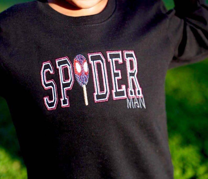 May include: Black long-sleeved shirt with the word "SPYDER" in white, outlined in black and pink, with a Spiderman mask graphic. The word "MAN" is below the word "DER".