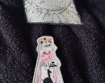 May include: A pink and white embroidered patch of a potion bottle with a black silhouette of a witch inside. The patch has a white border and a brown cork on top. The text "Magical Spells Stitches" is embroidered on a separate patch.