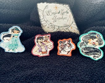 May include: Embroidered patches featuring characters from a popular animated film. The patches include a princess in a teal dress, a character with a monkey, a tiger, and another princess. A rectangular patch with the text "Magical Little Stitches" is also present.