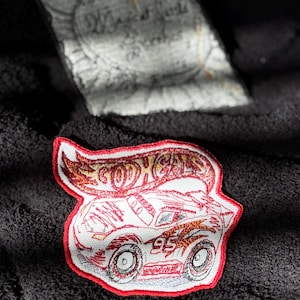 May include: Red and yellow embroidered patch with a red race car and the words "Hot Wheels" in white.