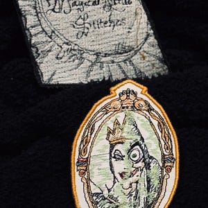 May include: Embroidered patch featuring the Evil Queen from Snow White, looking into a magic mirror with a golden frame. The text "Magical Mirror" is written on the patch.