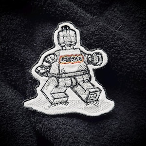 May include: A white embroidered patch of a Lego minifigure with the text "Let God" on the chest. The minifigure is walking with its arms outstretched.