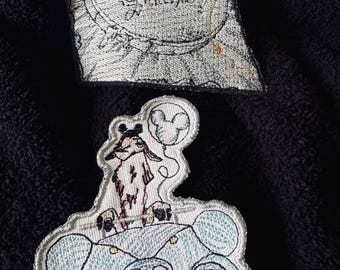 May include: Two embroidered patches. The first patch is white with black stitching and features the text "Magical Little Stitches". The second patch is white with black and blue stitching and features a cartoon character driving a blue car with a Mickey Mouse balloon.